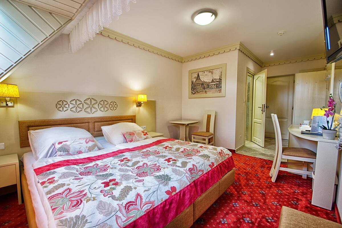 A bedroom with a bed, bedside lamps, a desk, and a chair.