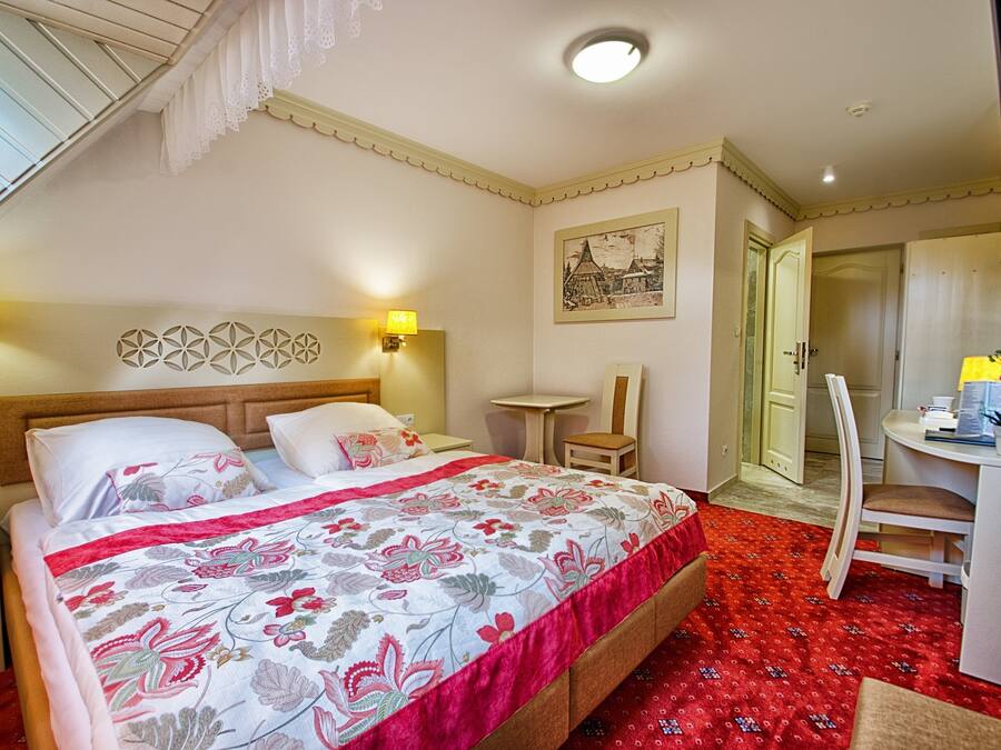 A bedroom with a bed, bedside lamps, a desk, and a chair.