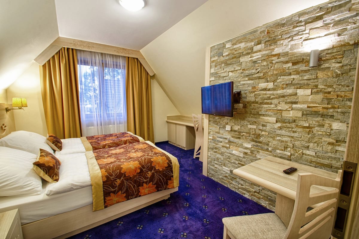 A hotel room with a bed, a desk, a TV, and a stone wall.