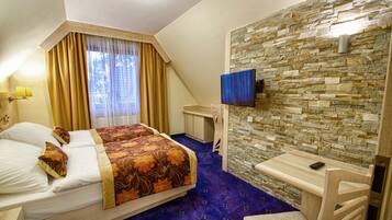 Una habitación de hotel con cama, escritorio, televisor y pared de piedra.