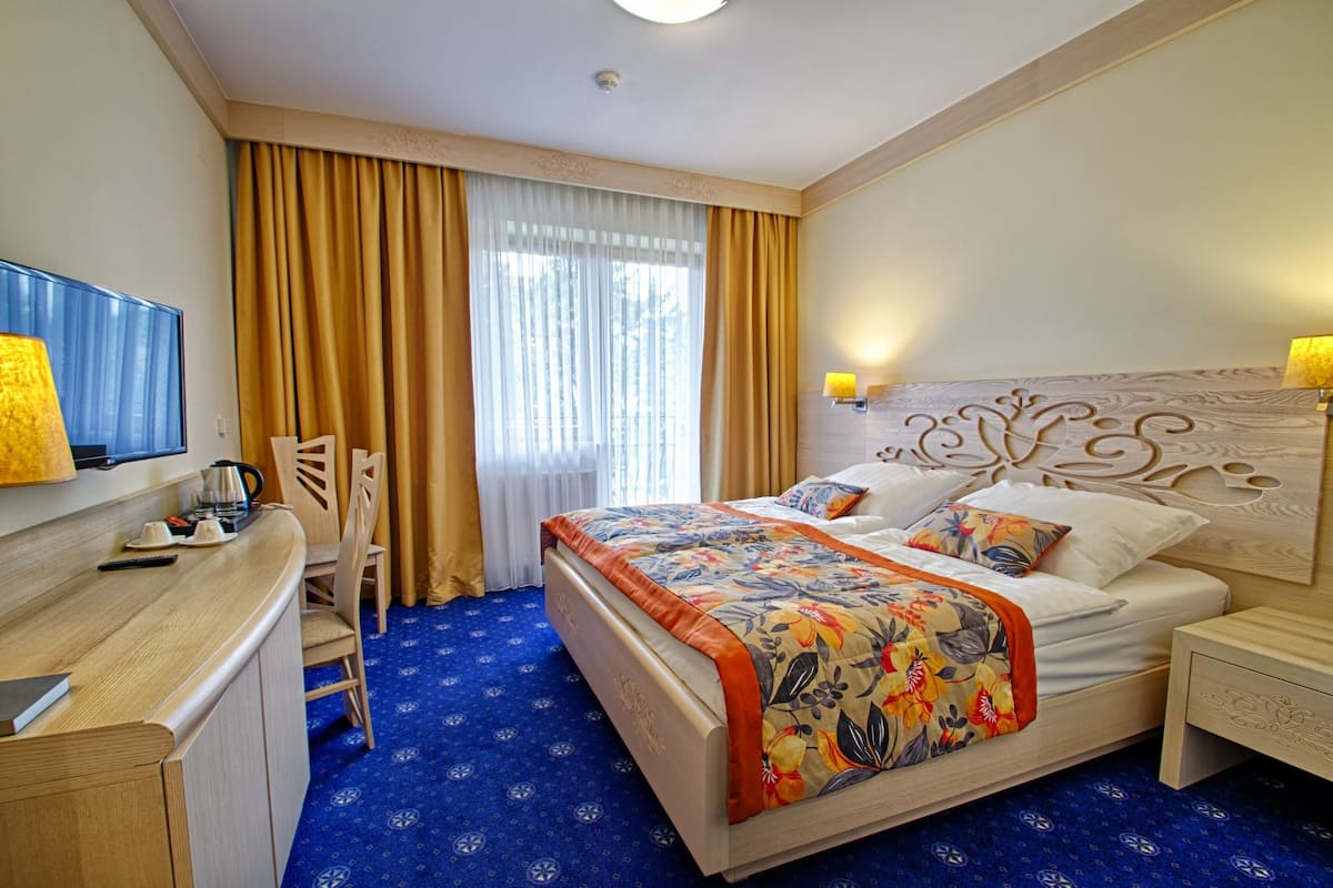 A hotel room with a bed, a desk, a chair, a television, and a window with curtains.