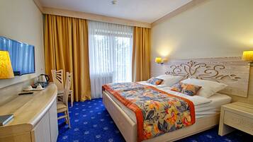 Una habitación de hotel con cama, escritorio, silla, televisor y ventana con cortinas.