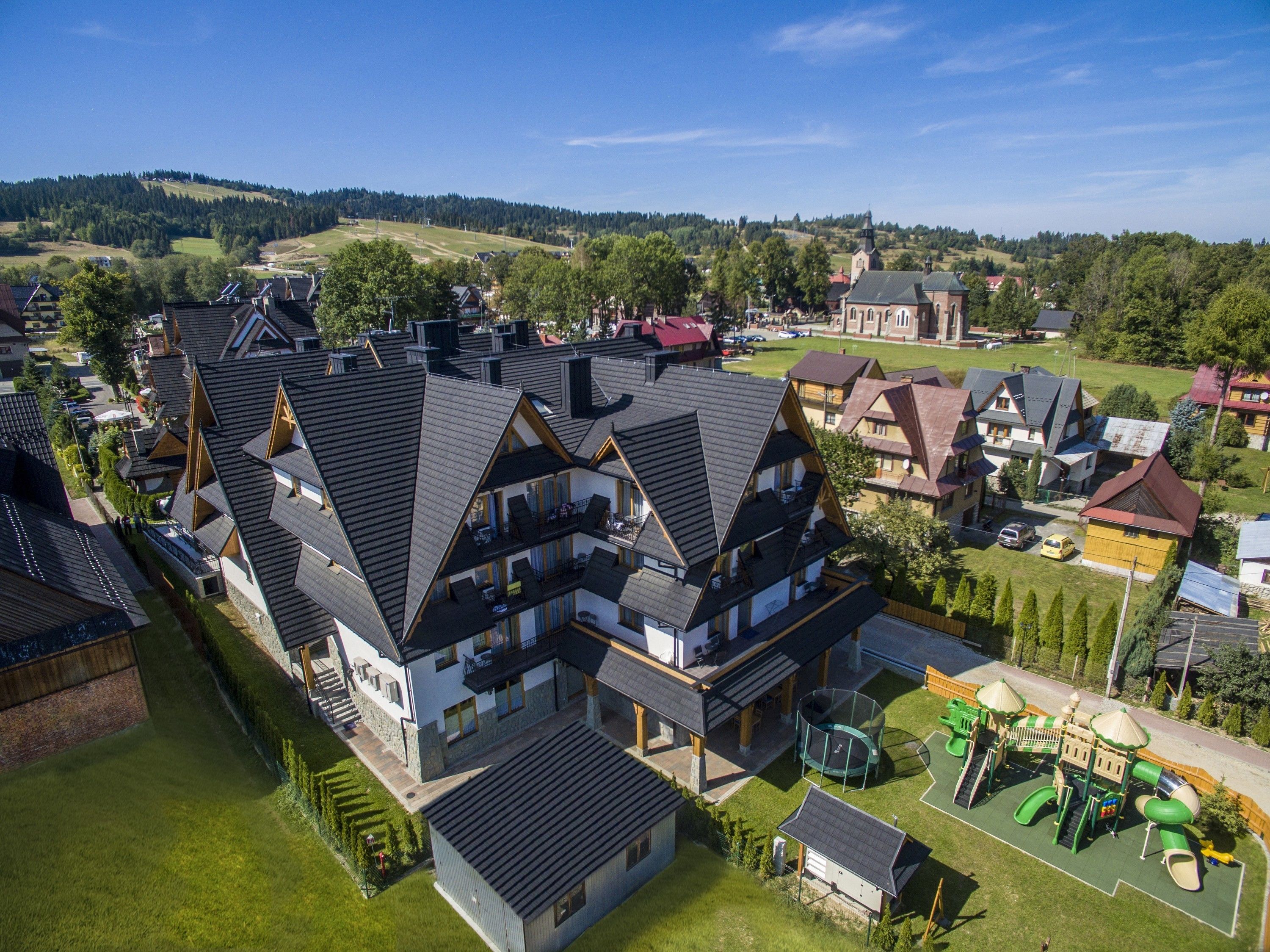 A modern multi-story house with a sloped roof, a large balcony, and a play area with a slide and climbing structure.