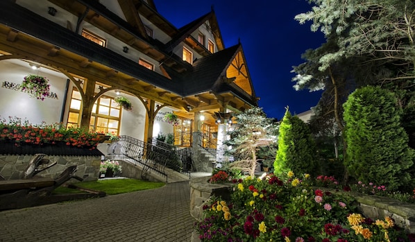 A traditional chalet with a stone facade, wooden beams, and a balcony with hanging flower baskets.