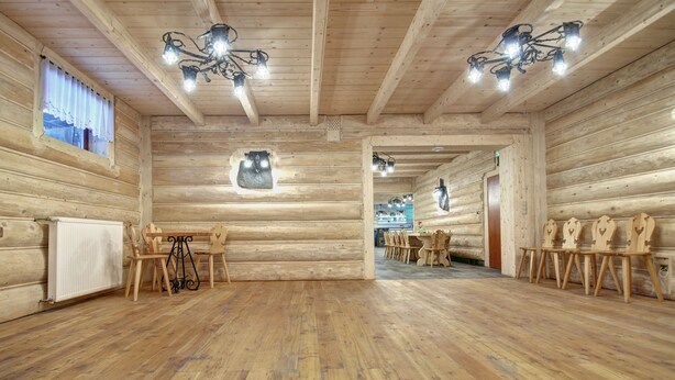 A log cabin interior with wooden walls, a wooden floor, a dining area with chairs, and a chandelier.