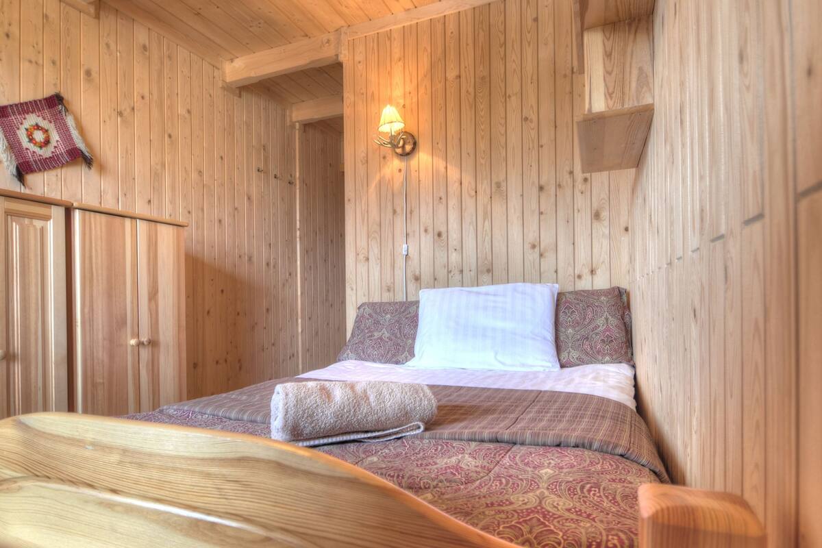 Ein Zimmer mit Holzwänden, einem Bett, einer Wandleuchte und einem kleinen Regal.