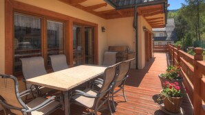 A wooden deck with a table and chairs, a grill, and potted plants.