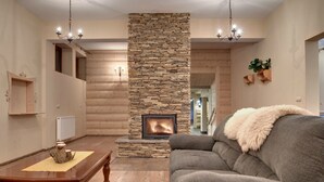 A cozy living room with a stone fireplace, wooden walls, a grey sofa, and a wooden coffee table.