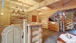 A log cabin interior with a wooden staircase, a chandelier, and a fireplace.