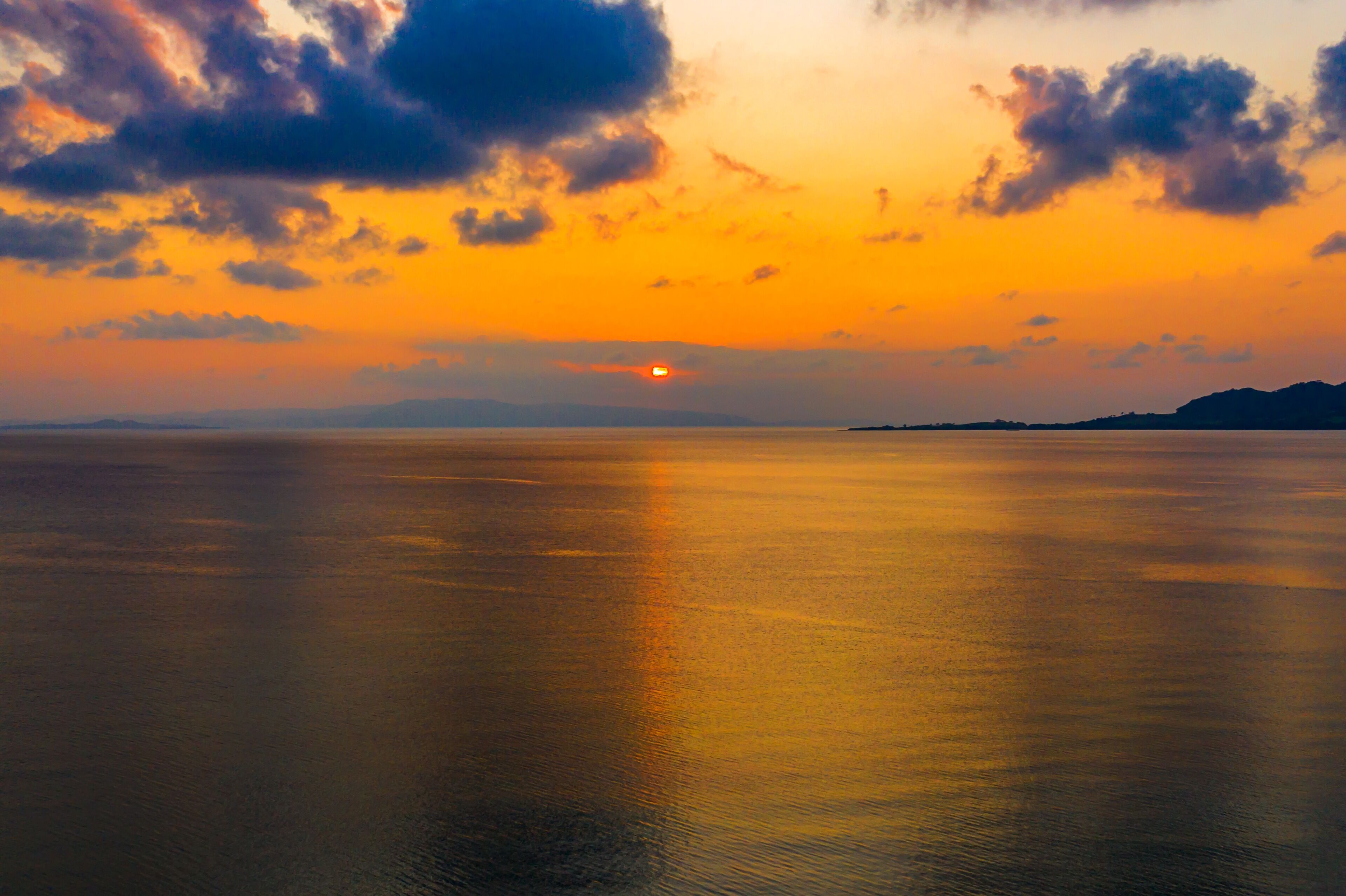 Mar tranquila al atardecer con cielo despejado y formas de tierra lejanas.