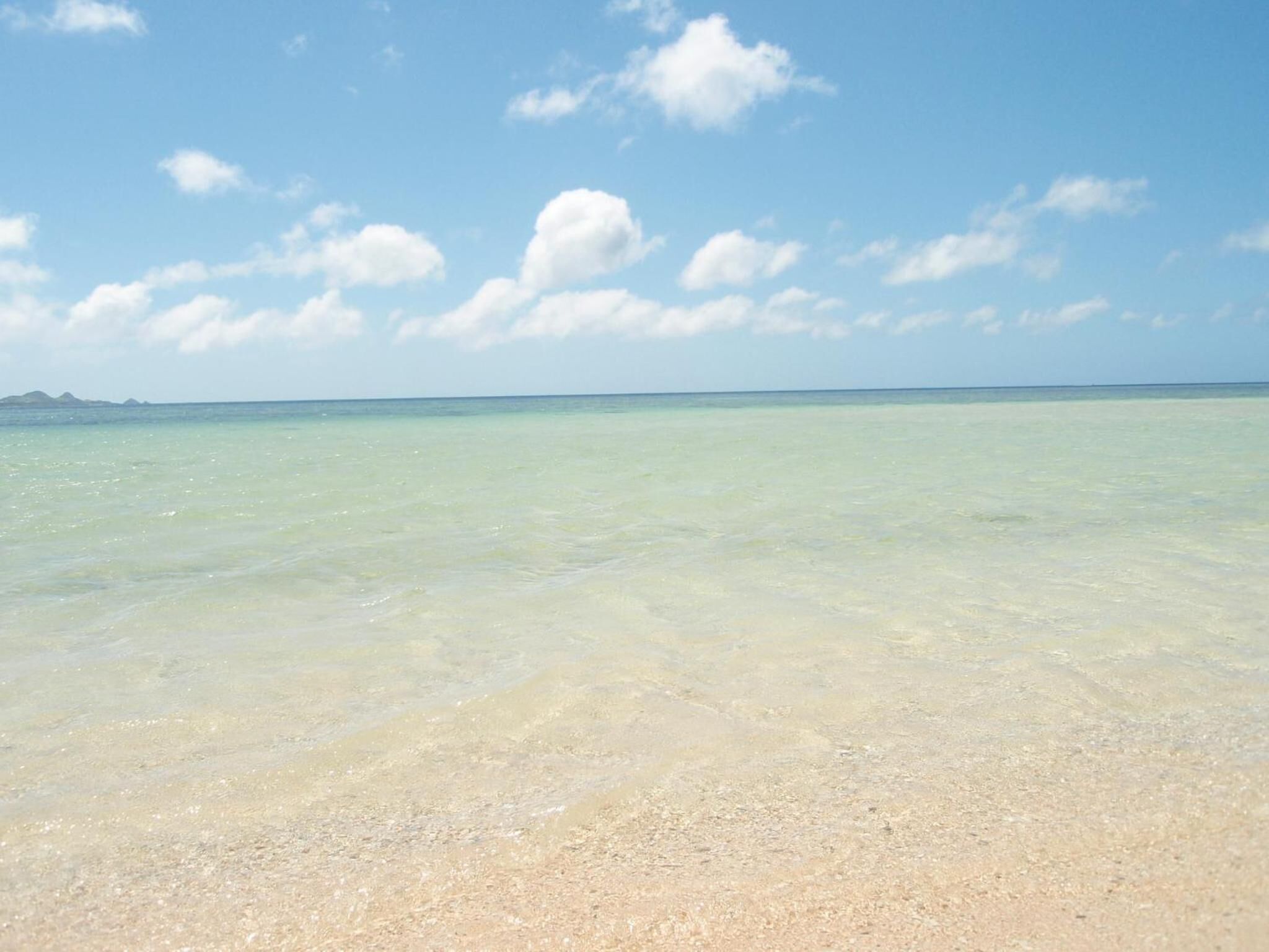A beach with clear shallow waters and a distant mountain range.