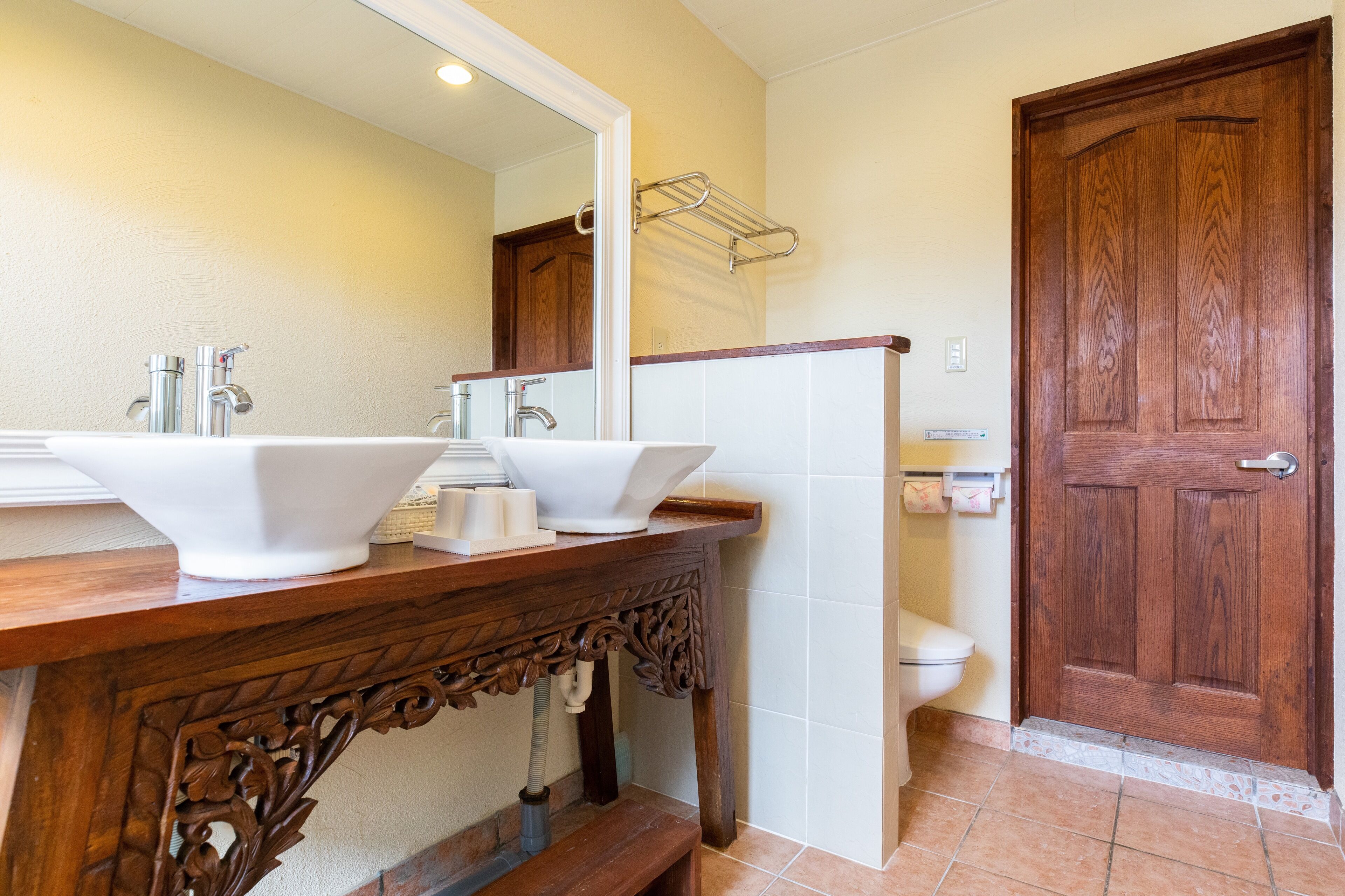 A bathroom with two sinks, a wooden vanity, a large mirror, a wooden door, and a toilet.