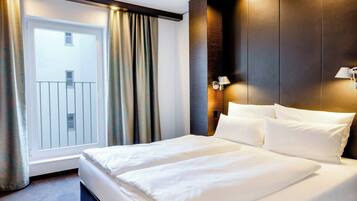 Una habitación de hotel con una cama grande, una ventana con cortinas y una lámpara fijada a la pared.