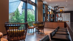 Interior moderno com piso de madeira, área de bar com assentos e vista para um edifício com torre através de grandes janelas.
