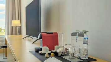 Habitación de hotel con escritorio, cafetera, tazas, botella de agua y jarra de vidrio.