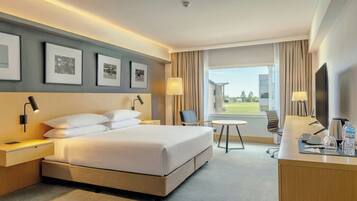 Quarto de hotel com cama, mesas de cabeceira, escrivaninha, cadeira, televisão e janela com vista.