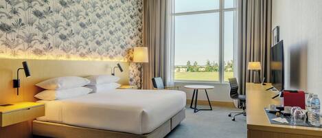 A hotel room with a large bed, a desk with a chair, a TV, and a window with curtains.