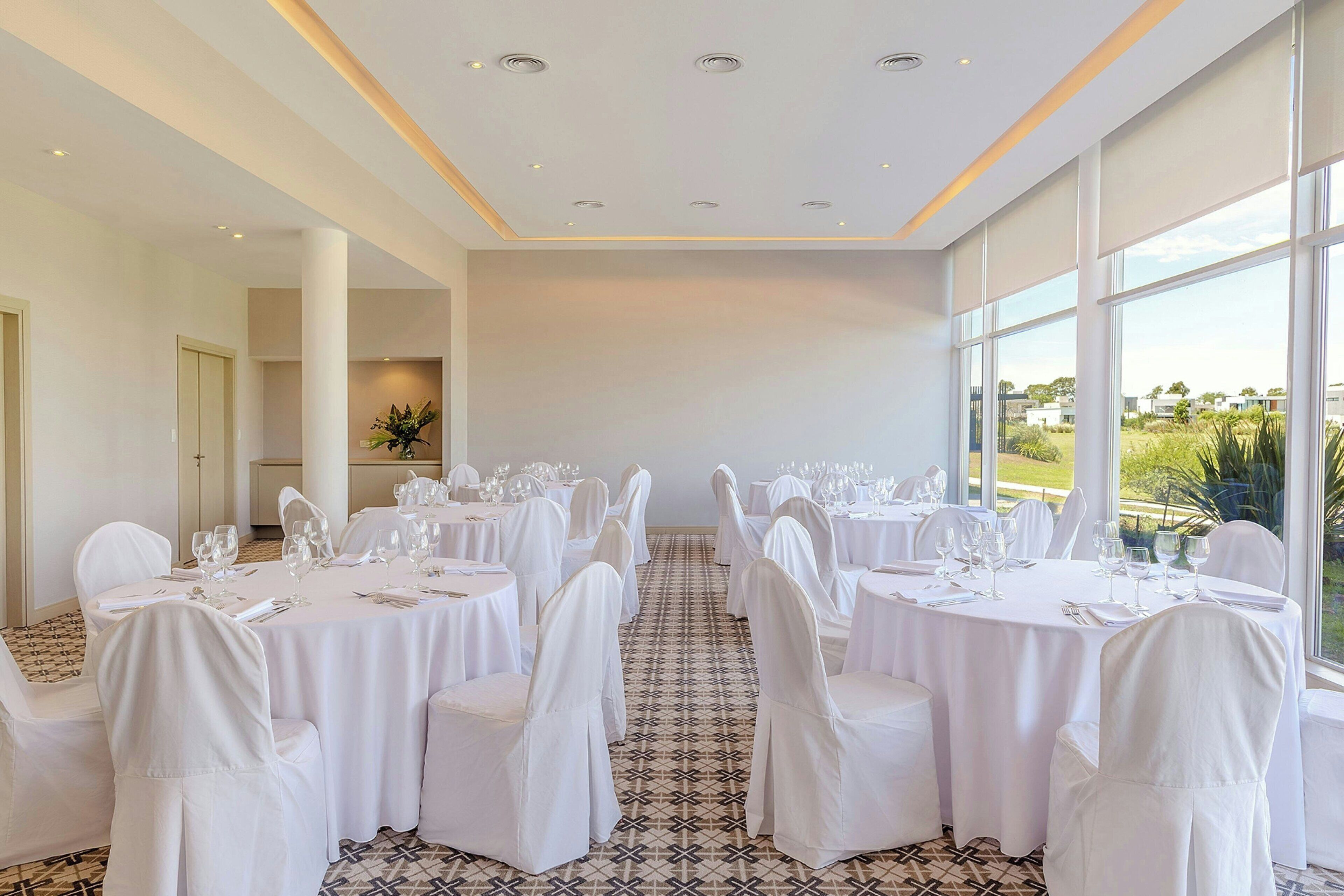 A conference room with round tables, white chairs, and a large window offering a view of the outdoors.