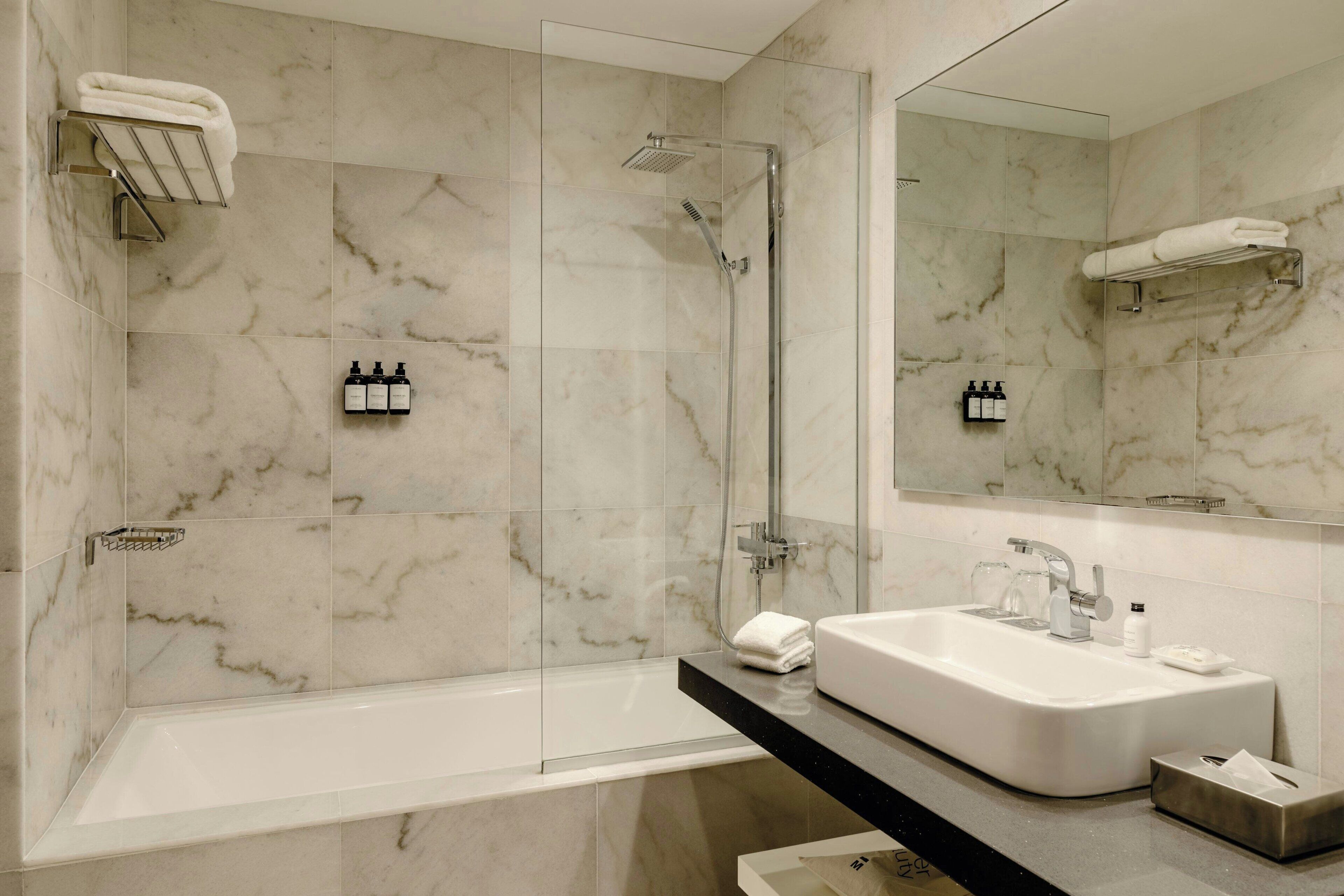 A modern bathroom with a glass-enclosed shower, a white sink, and marble walls.