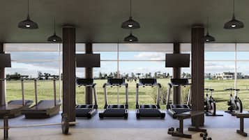Une salle de sport équipée de tapis de course, de vélos elliptiques et de poids libres, avec de grandes fenêtres donnant sur un parc.