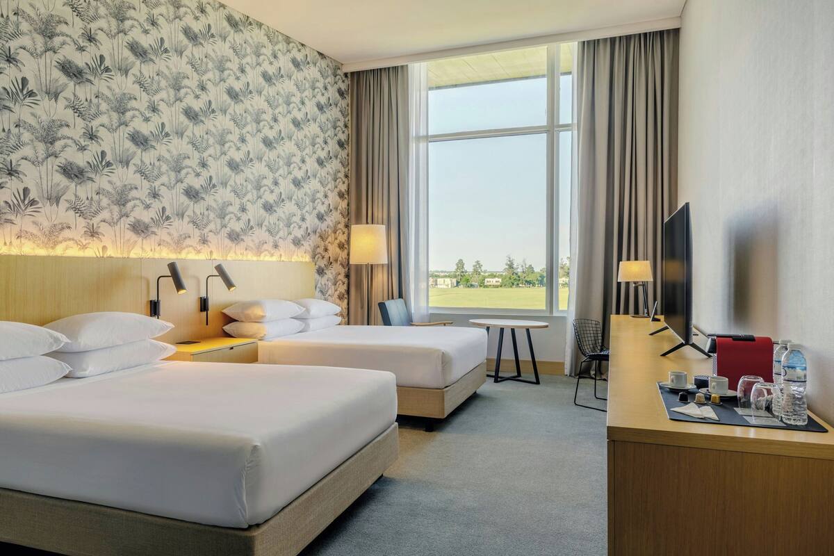 A hotel room with two beds, a desk, a TV, and a window with a view.