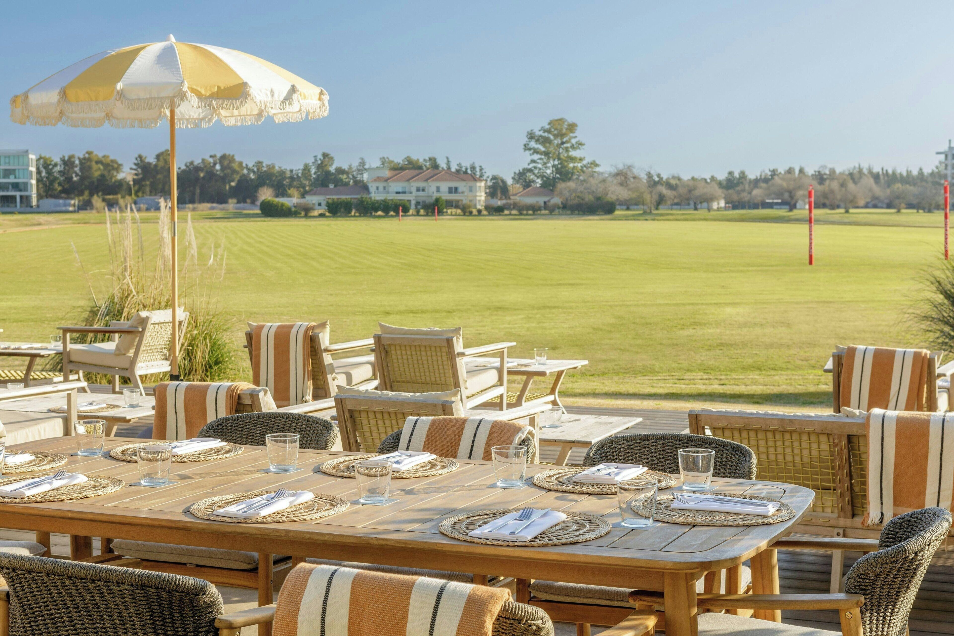 A dining area with a table set for four, outdoor chairs, and a large umbrella.