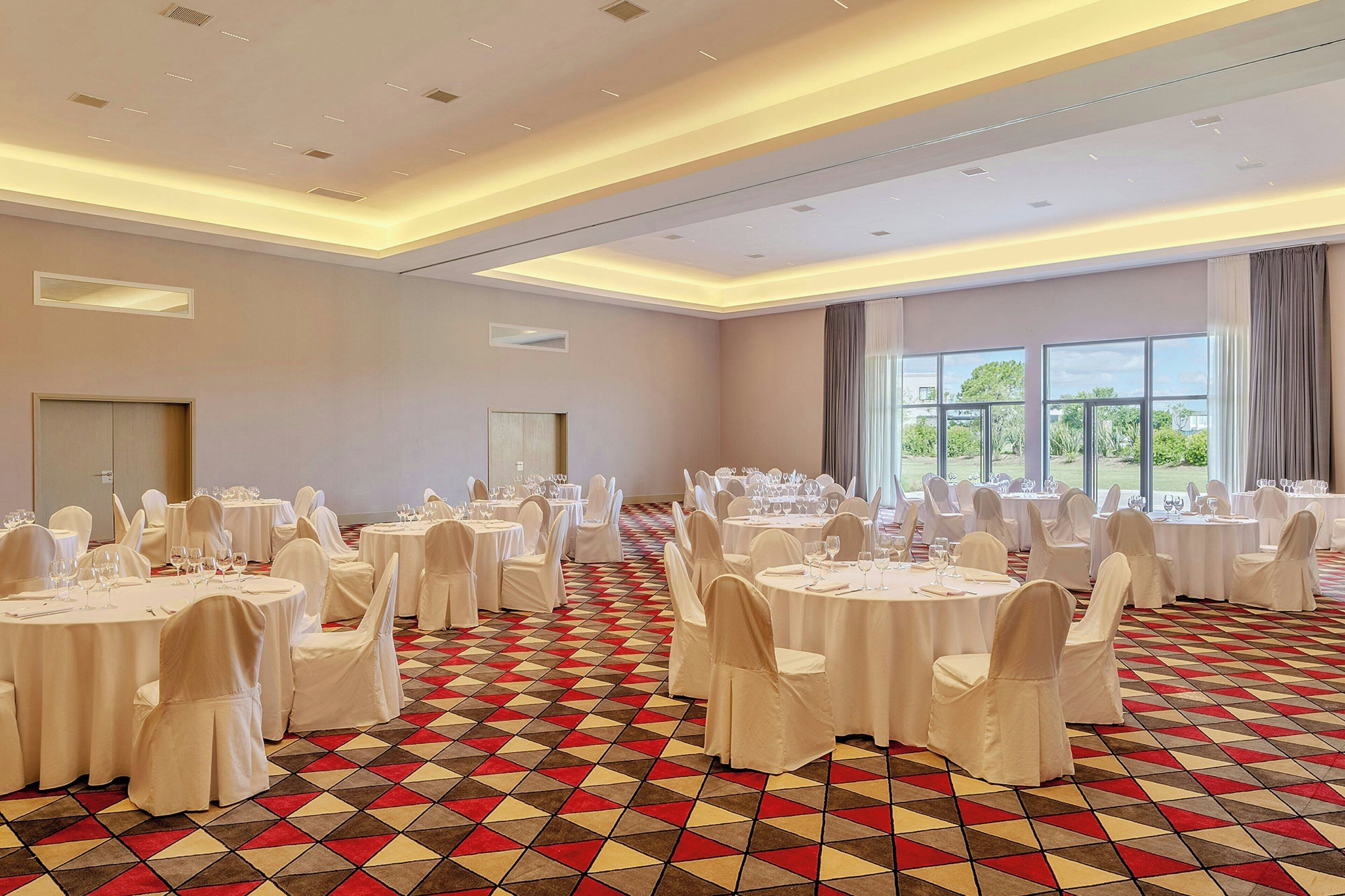 A banquet hall with round tables, white chairs, and a patterned carpet.