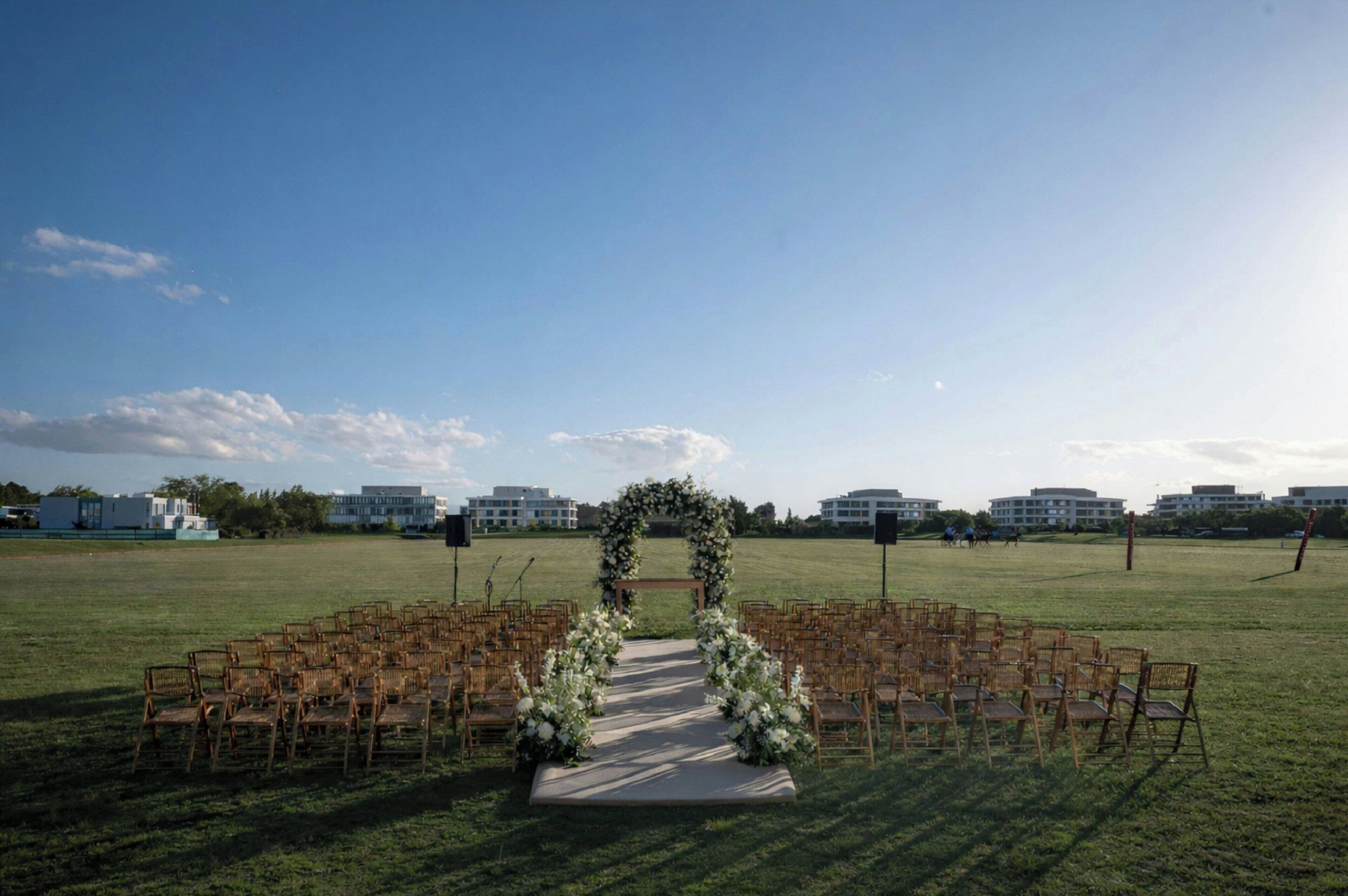Une cérémonie de mariage en plein air, avec une arche décorée de fleurs et des rangées de chaises en bois.