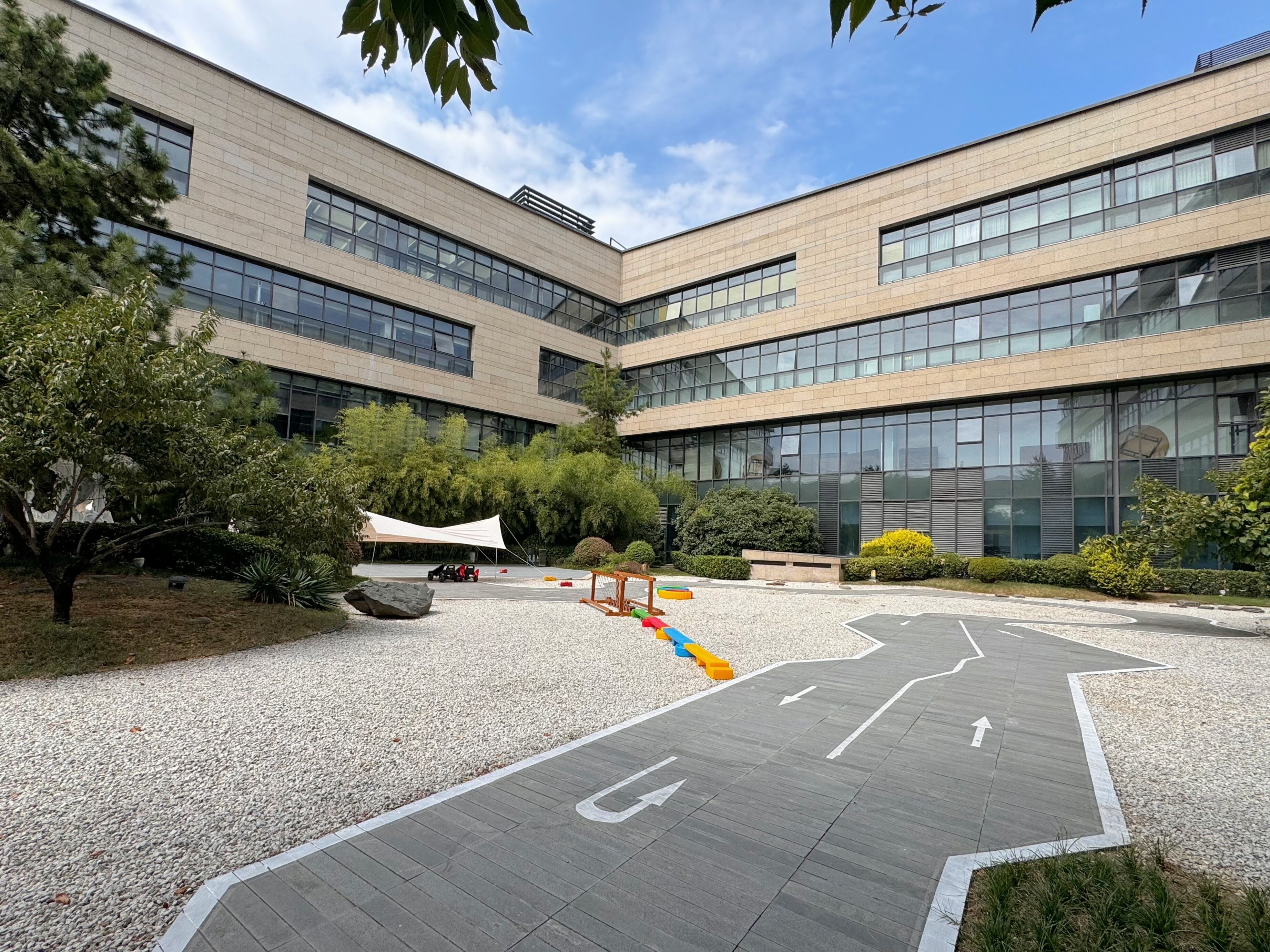 A modern building with a courtyard featuring a playground, a covered seating area, and a gravel path.