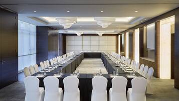 A conference room with a long table, white chairs, and a projector screen.