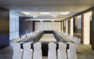 A conference room with a long table, white chairs, and a projector screen.