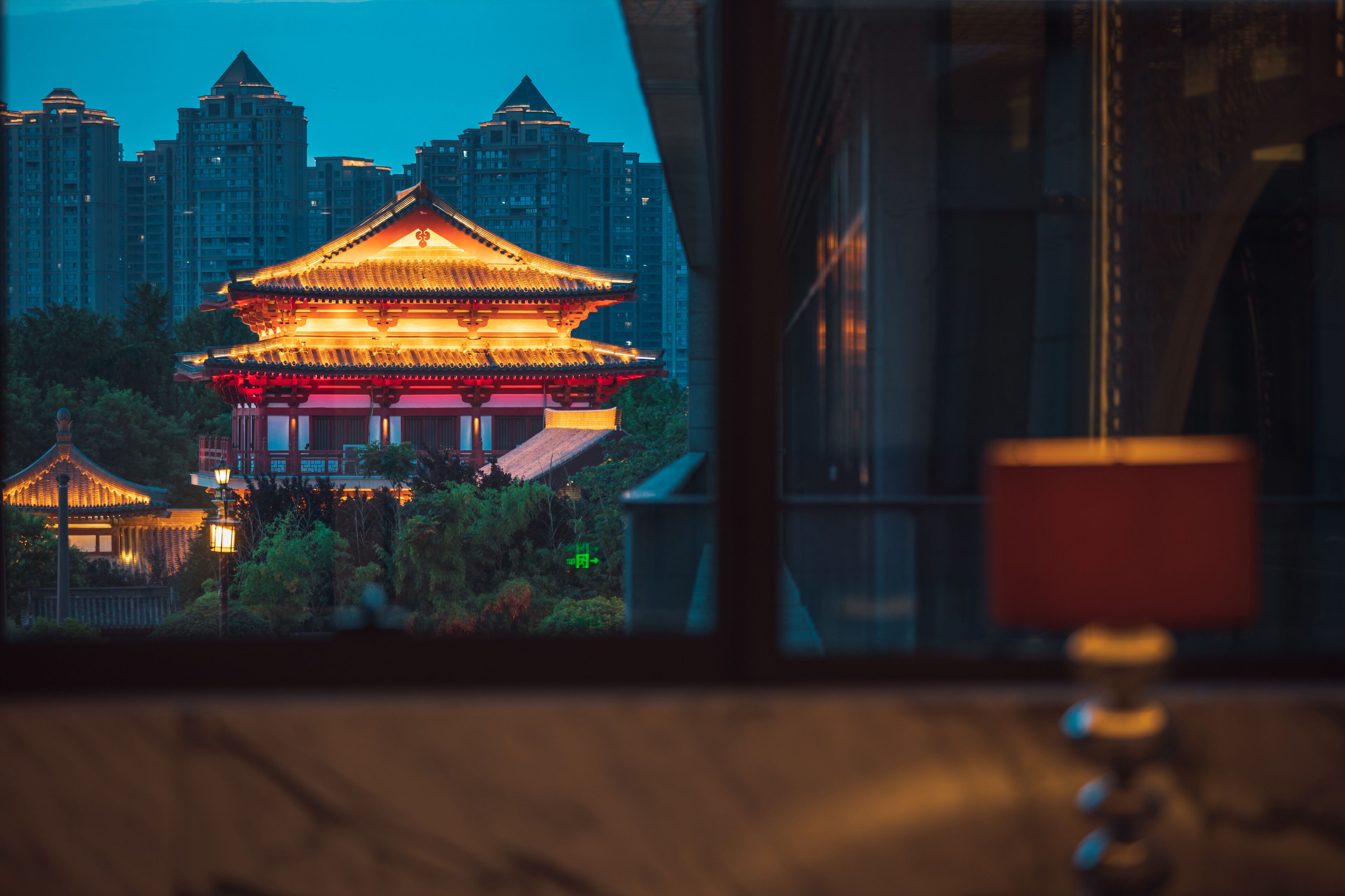 A traditional building with a golden roof, surrounded by greenery and modern high-rise buildings in the background.