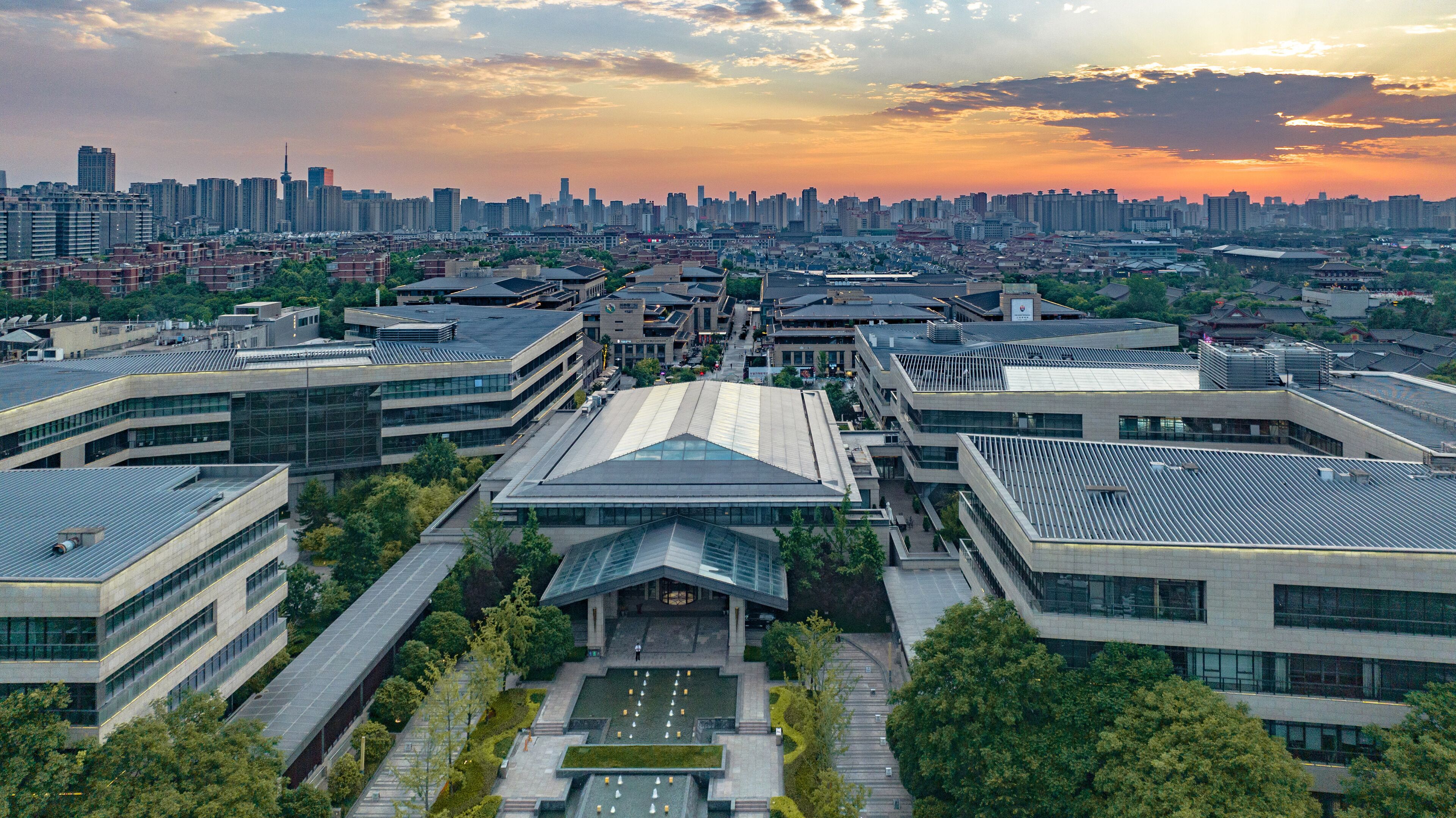 A modern building complex with multiple structures, including a central building with a unique roof design and surrounding buildings with flat roofs.