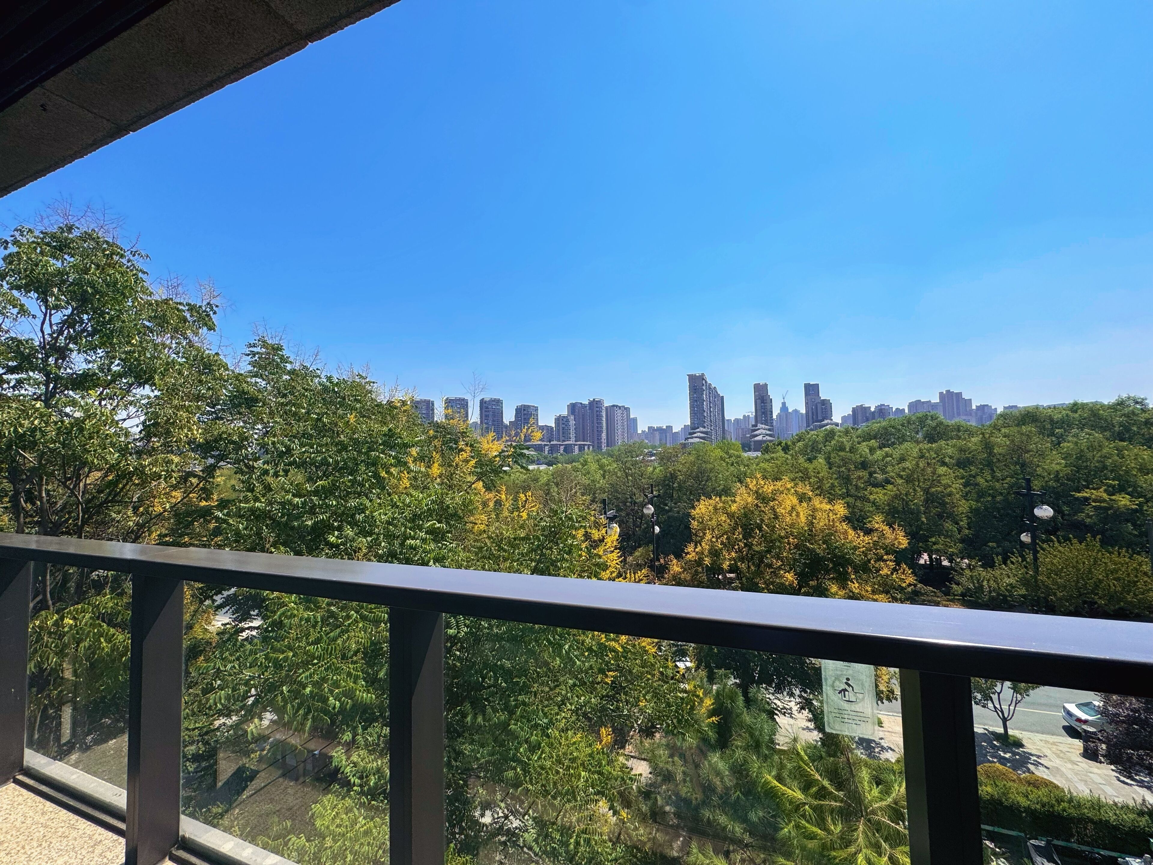 Vista desde un balcón sobre un paisaje urbano con edificios altos y árboles verdes frondosos.