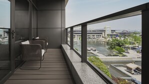 Un balcón con mobiliario de mimbre y vistas a un paisaje urbano que incluye un edificio grande con letreros de "VICHY".
