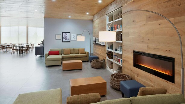 A modern living room with a fireplace, wooden walls, and a bookshelf. - Country Inn & Suites by Radisson, Katy (Houston West), TX (Katy)