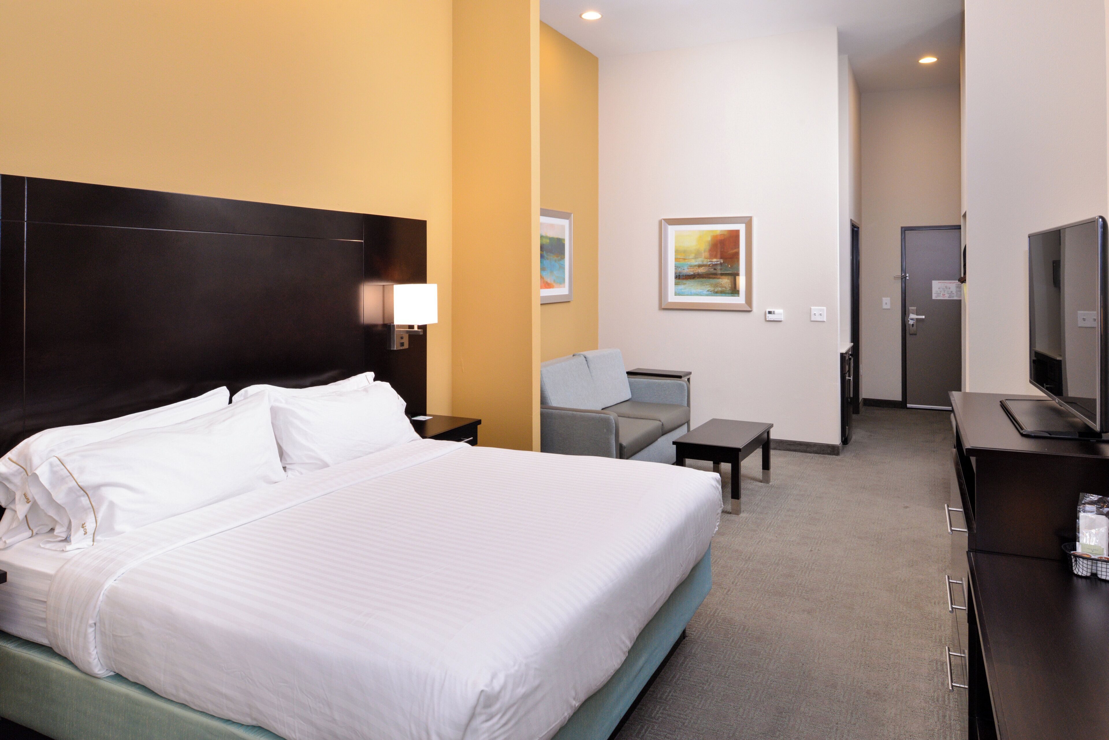 Ein Hotelzimmer mit einem großen Bett, einem Schreibtisch, einem Sessel, einem Fernseher und einer Tür zu einem Badezimmer.