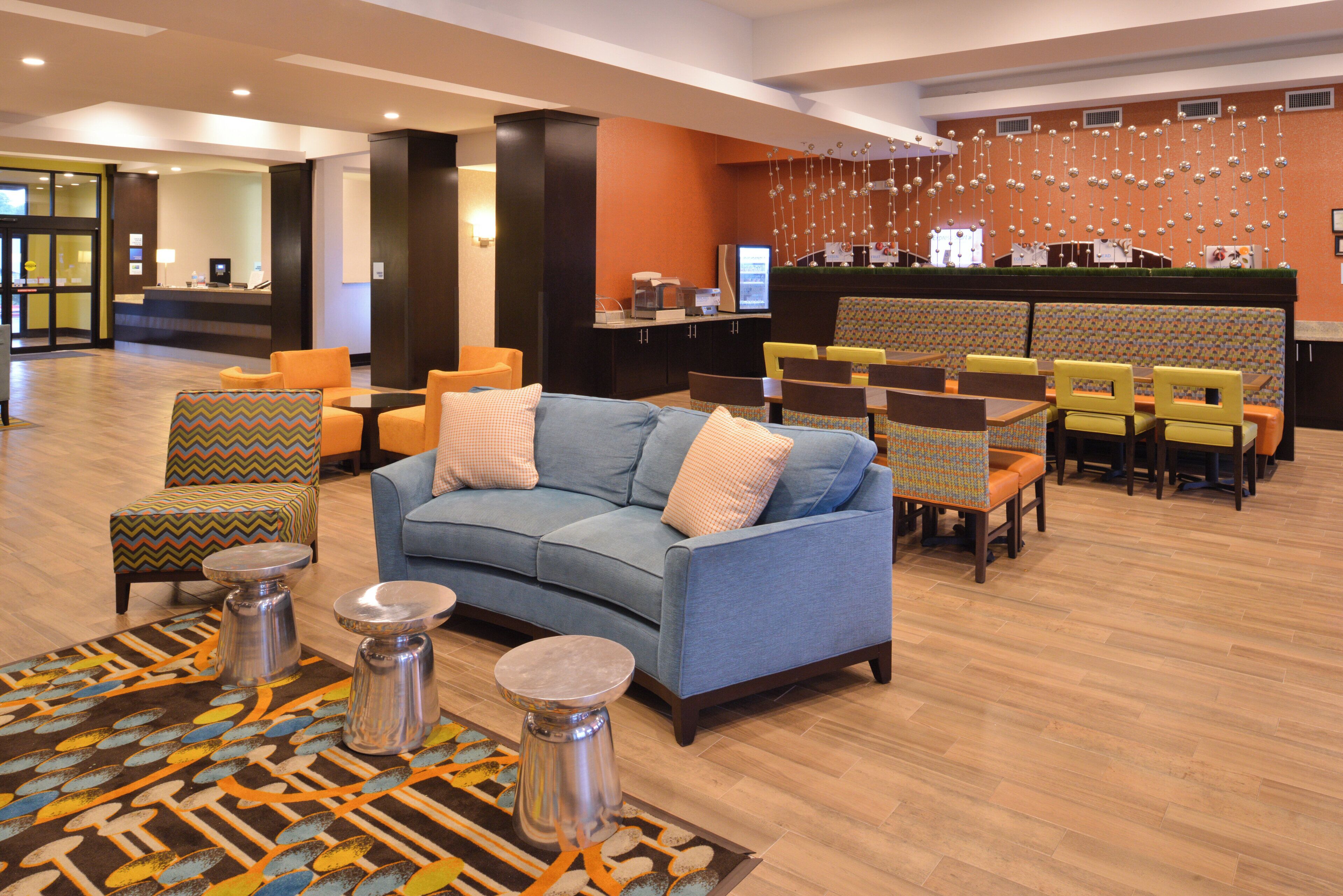 Un hall d’entrée avec un canapé bleu, des fauteuils à motifs, un comptoir d’accueil et un mur orné de décorations suspendues.