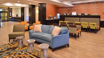 Eine Lobby mit einem blauen Sofa, gemusterten Sesseln, einem Empfangstresen und einer Wand mit Wanddekorationen.