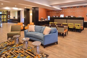A lobby with a blue sofa, patterned chairs, a reception desk, and a wall with hanging decorations.