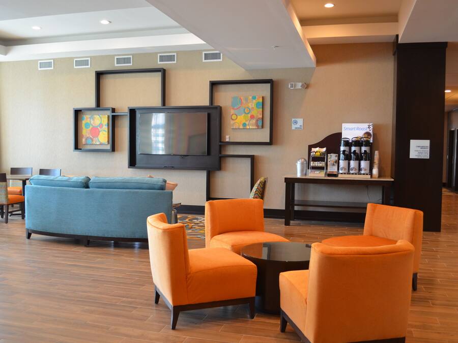 Un vestíbulo de hotel con un sofá azul, sillas naranjas, un televisor, obras de arte enmarcadas y una estación de café.