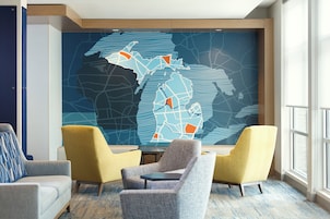 A modern hotel lobby with a large map mural, comfortable seating, and a view of the city through large windows.