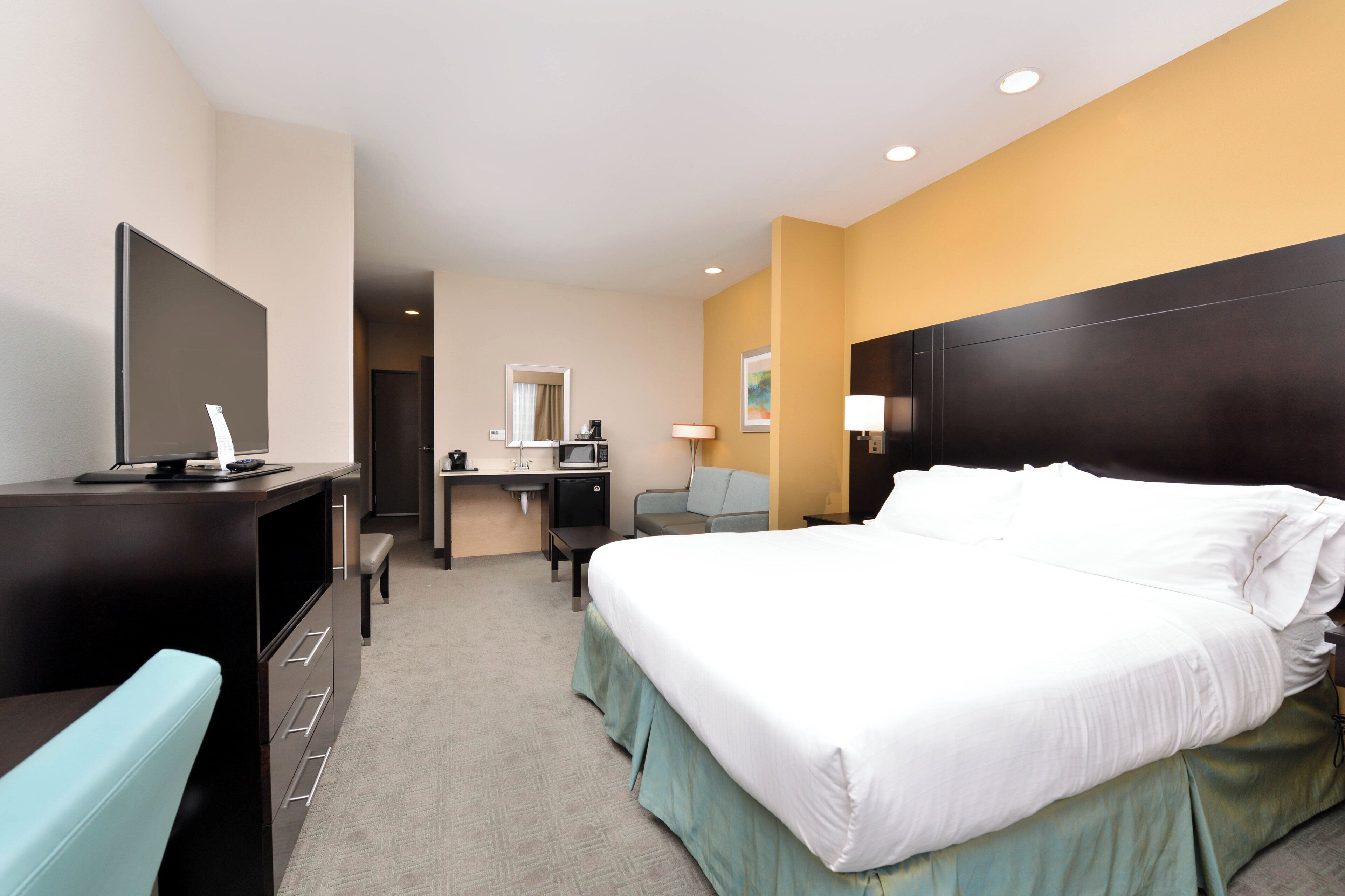 A hotel room with a bed, desk, chair, television, and a small kitchenette.
