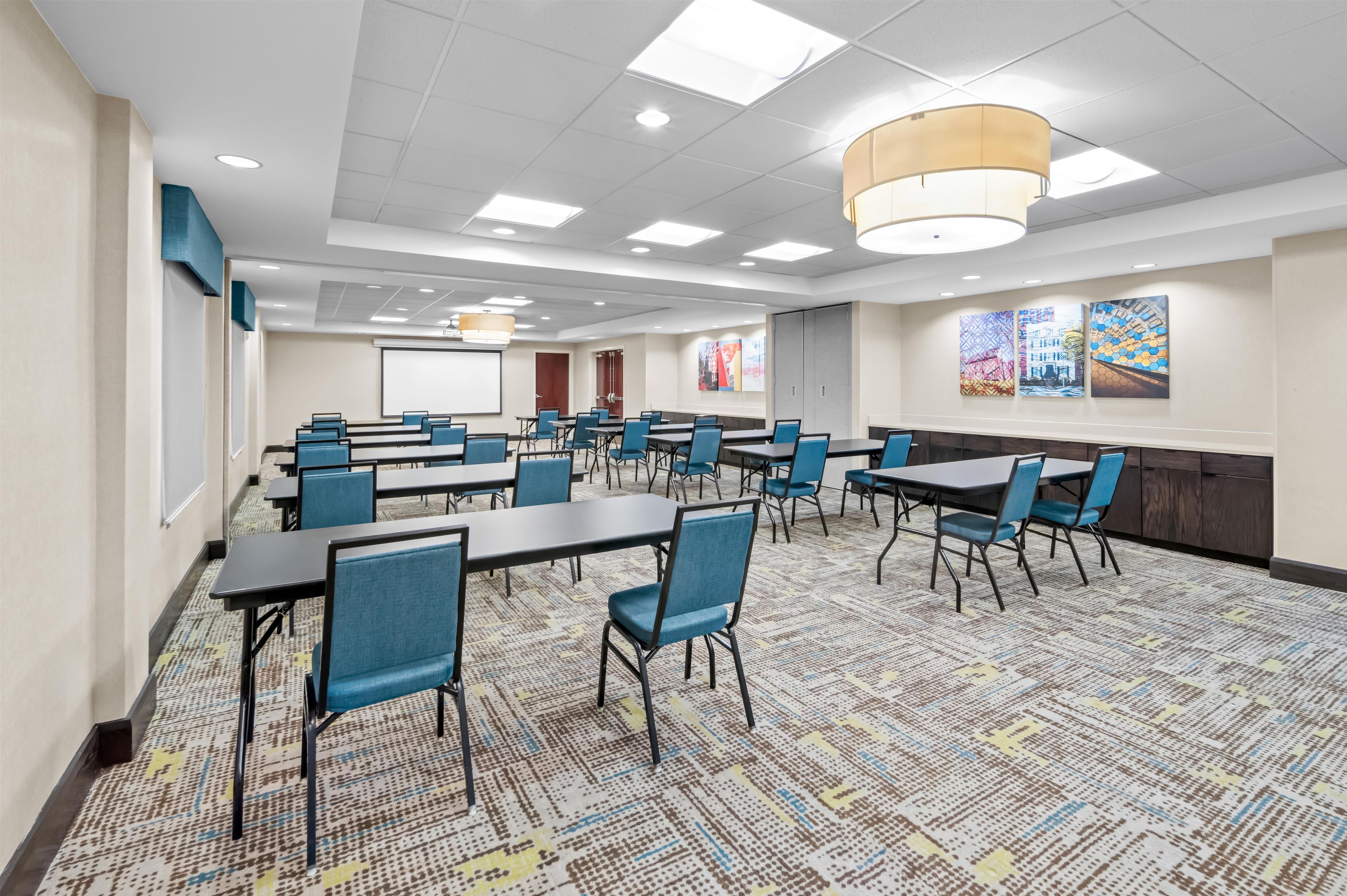 A conference room with multiple tables and chairs, a projector screen, and a large window.