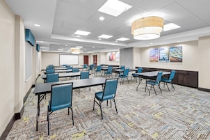 A conference room with multiple tables and chairs, a projector screen, and a large window.