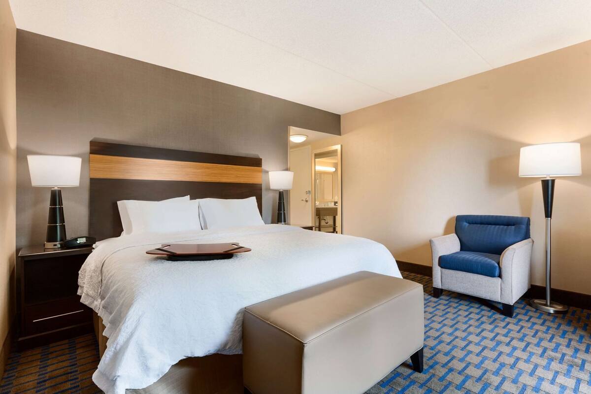 A hotel room with a bed, bedside tables, a chair, a floor lamp, and a mirror.