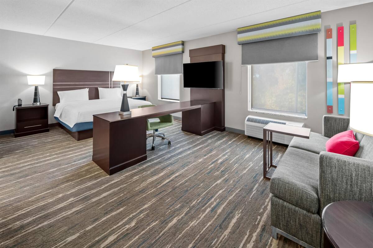 A hotel room with a bed, desk, chair, TV, and a sofa.
