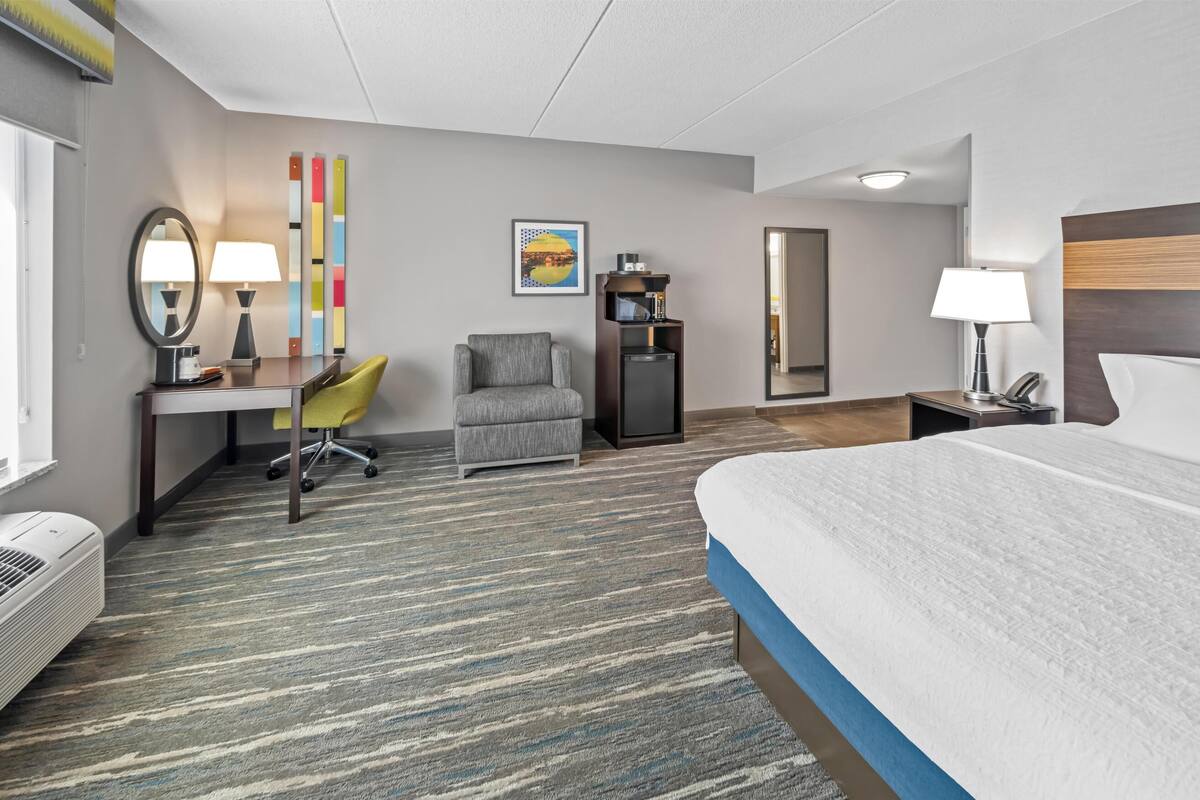A hotel room with a bed, desk, chair, and a small kitchenette.