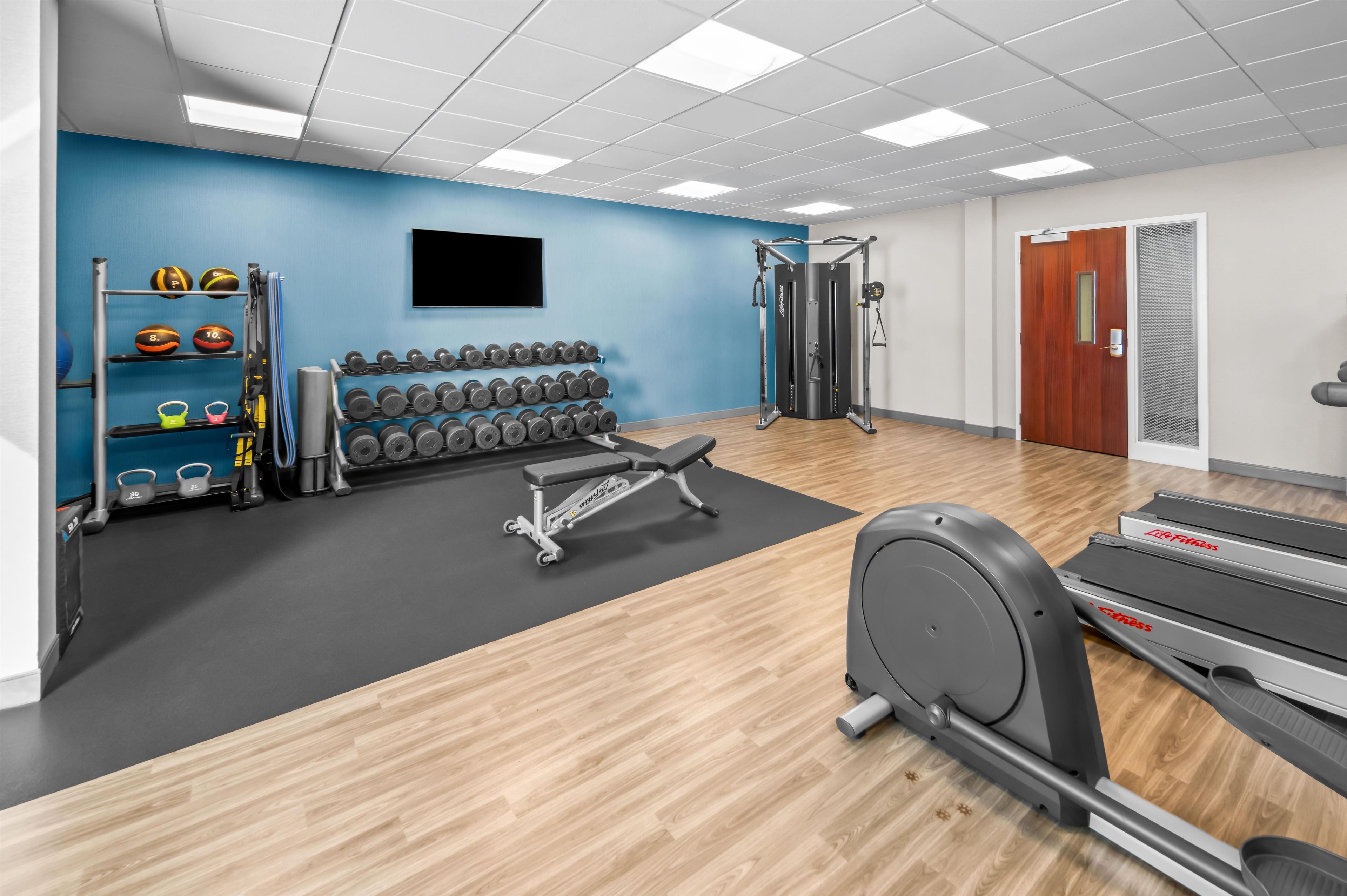 A gym with exercise equipment, a wall-mounted TV, and a door with a window.