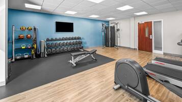 A gym with exercise equipment, a wall-mounted TV, and a door with a window.